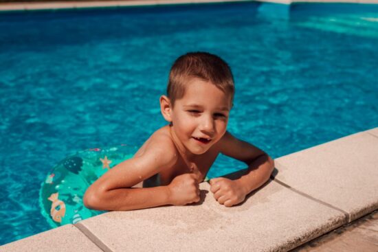 Young boy pulling himself out of the swimming pool