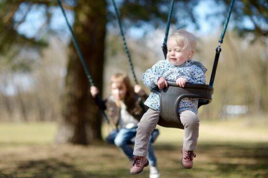 a toddler and a young girl swinging at a playground